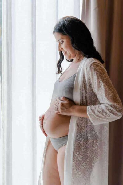 Grávida com robe de renda branco para sessão fotográfica de maternidade e baby shower.
