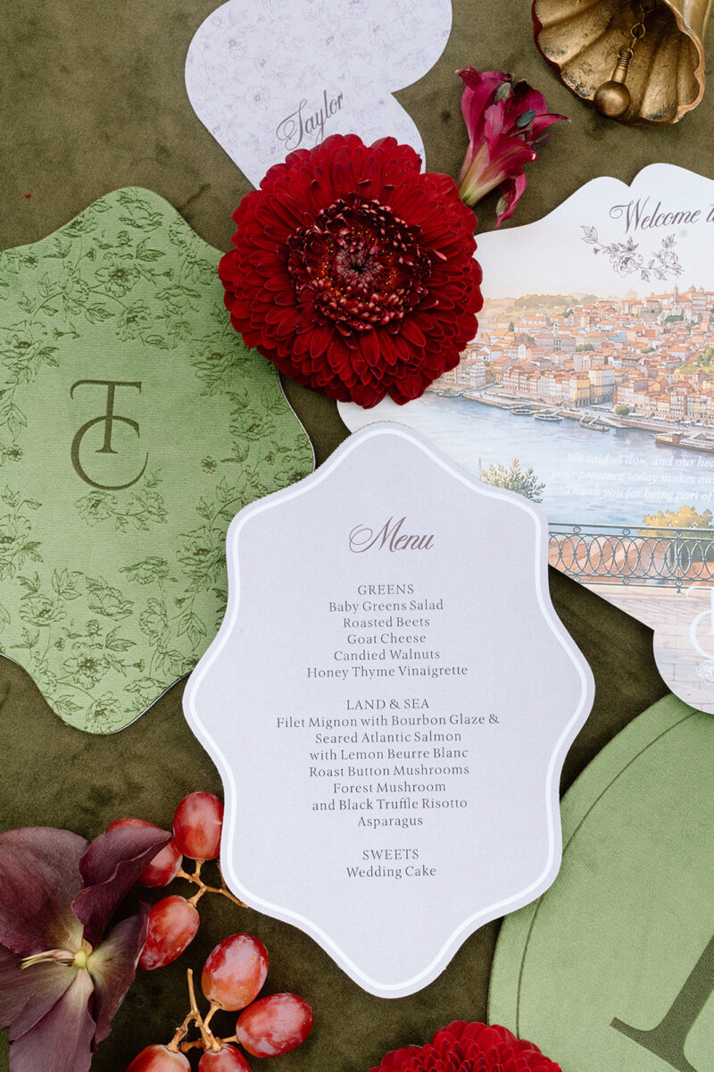 Menu de casamento em veludo verde com monograma gravado e menu em papel branco recortado, com dálias bordeaux e uvas