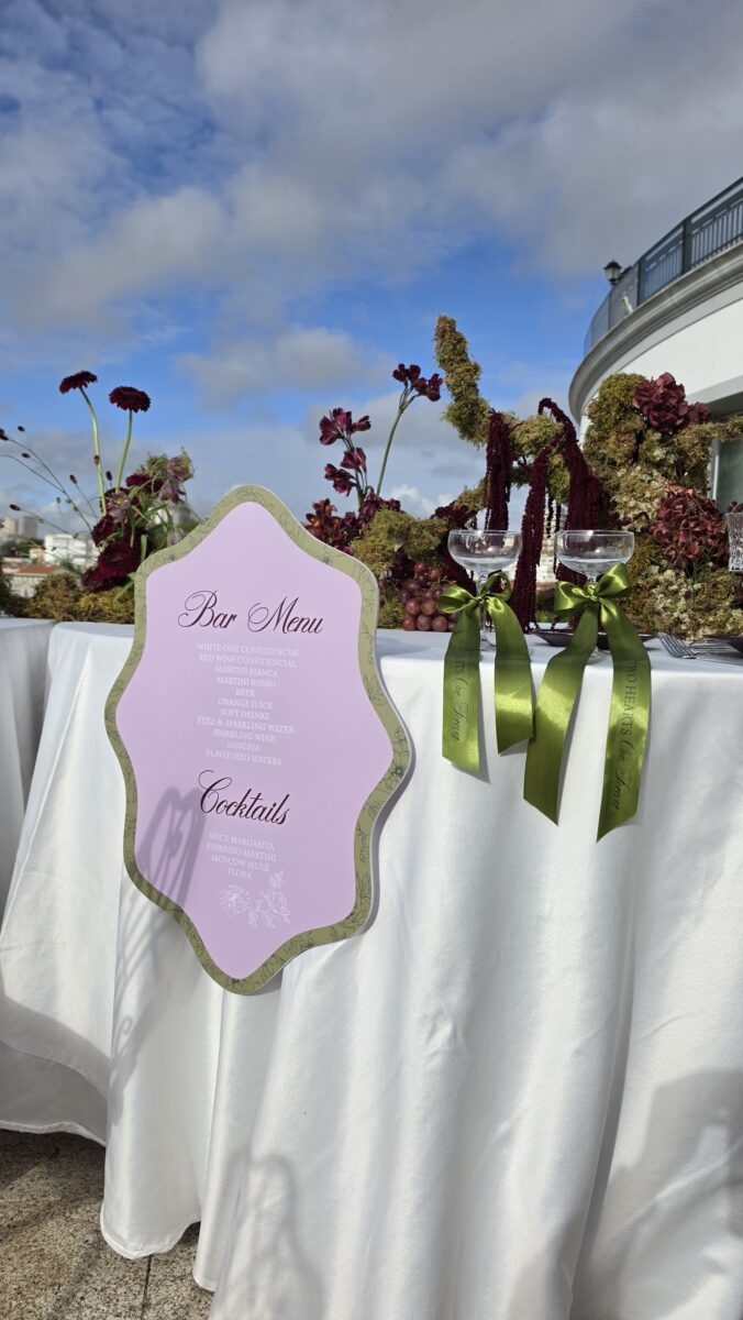 Menu bar de casamento em lilás com moldura verde num terraço com flores bordeaux e taças com fitas verdes